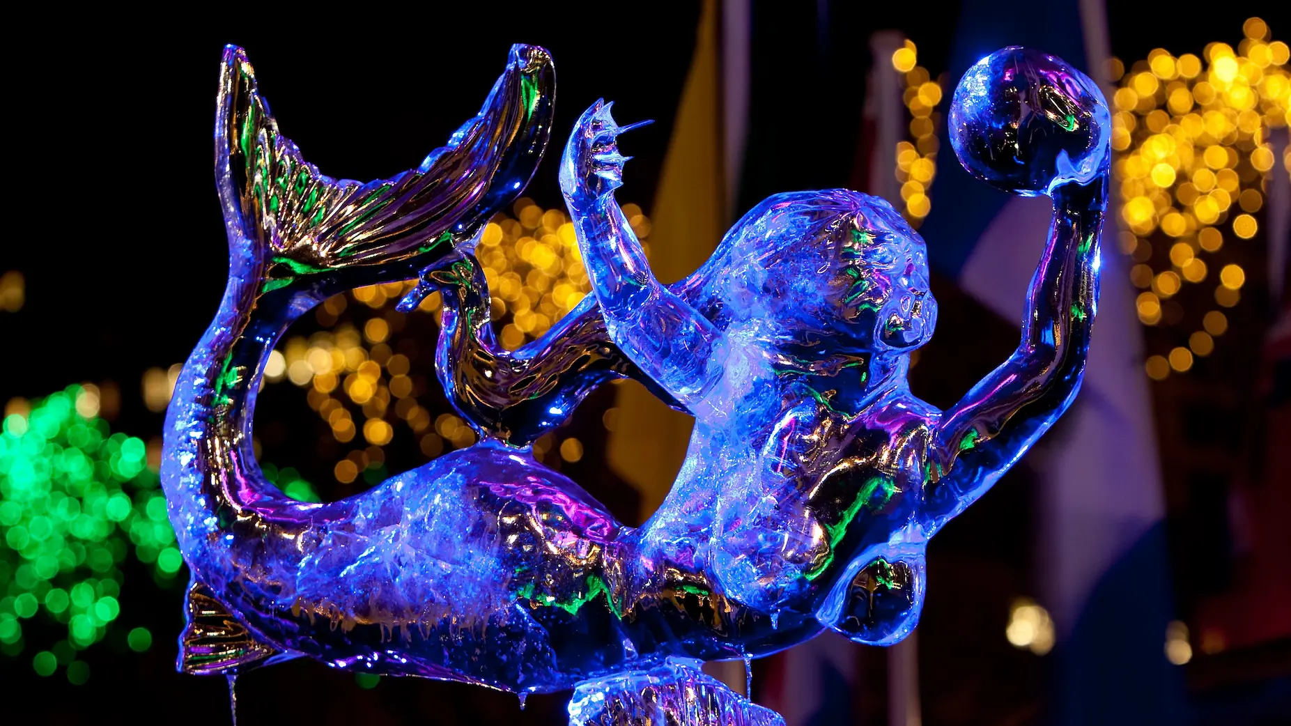A mermaid sculpture made of glass, shining in a blue light, displayed at an occasion.